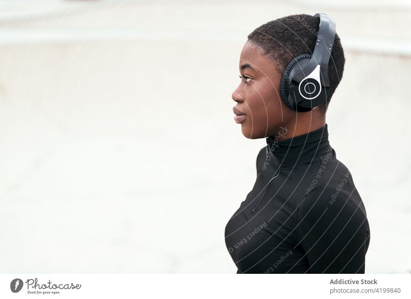 Verträumte schwarze Frau mit Headset, die auf einer Plattform ruht Kurze Haare Kopfhörer Musik zuhören reflektierend verträumt trendy Gesang Porträt benutzend