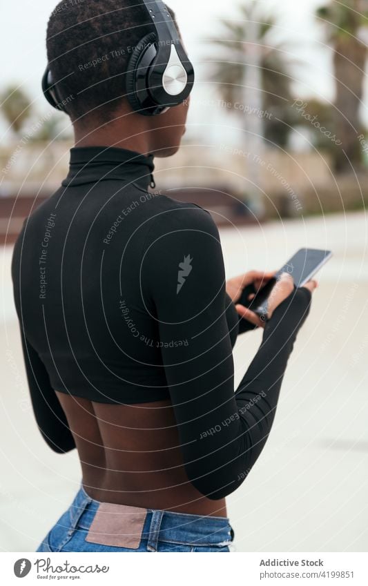 Rückansicht einer schwarzen Frau, die in der Stadt mit ihrem Smartphone im Internet surft Textnachrichten schwarzer Bildschirm Kurze Haare online Zeitvertreib