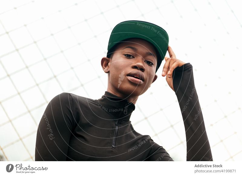 Coole schwarze Frau mit Mütze am Gitterzaun Individualität cool Stil mit dem Finger nach oben zeigen trendy Verschlussdeckel Zaun Großstadt Porträt Raster