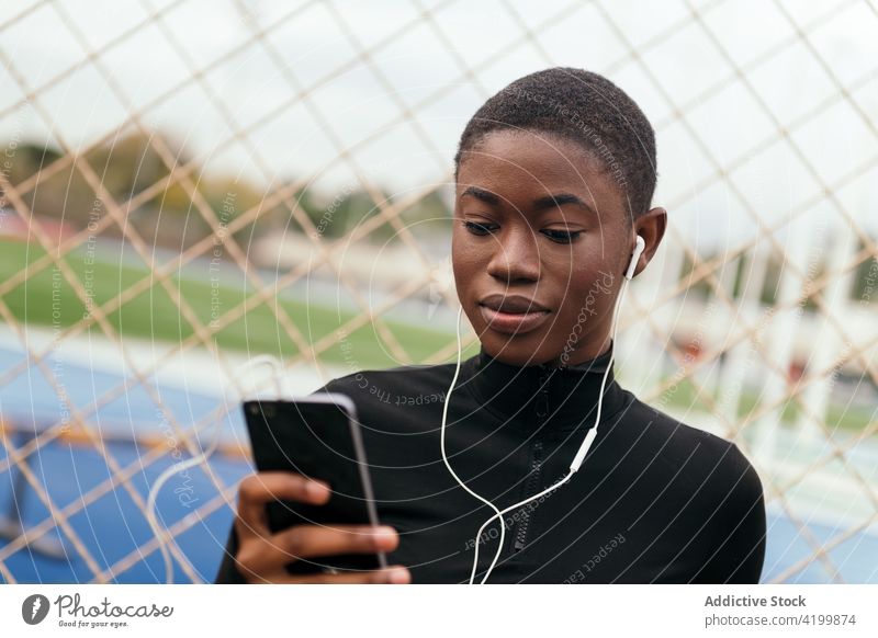 Aufmerksame schwarze Frau mit Kopfhörern, die in der Stadt mit ihrem Smartphone chattet Kurze Haare plaudernd Musik zuschauend zuhören Internet Porträt