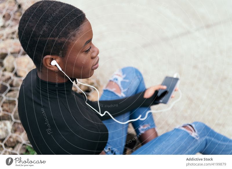 Kurzhaarige schwarze Frau, die mit einem Mobiltelefon und Kopfhörern Musik hört Afroamerikaner Smartphone Headset Gesang zuhören Kurze Haare Porträt benutzend