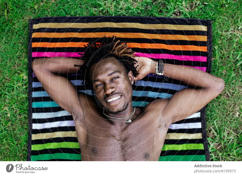 Lächelnder schwarzer Mann entspannt sich auf einem Handtuch im Gras Lügen Sommer Urlaub genießen sorgenfrei sich[Akk] entspannen männlich ethnisch