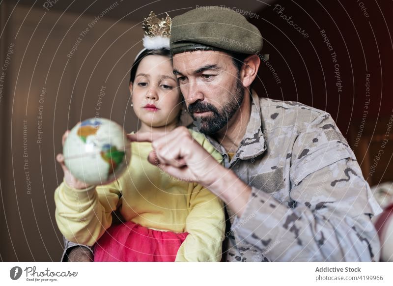 Militärischer Vater, der auf einen Ort auf dem Globus zeigt Tochter reden Krieg Händchenhalten wehren Patriotin Soldat Armee Mann Mädchen Uniform Sicherheit