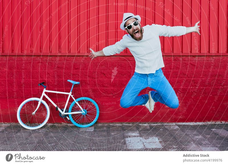 Hipster-Mann springt in der Nähe von Fahrrad auf Stadtstraße Mitfahrgelegenheit Straße Radfahrer trendy Großstadt Gebäude männlich Vollbart Outfit