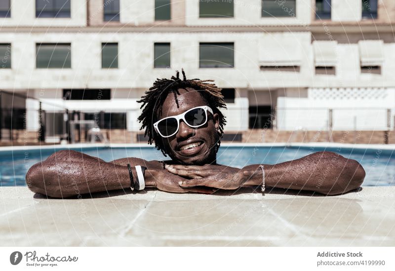 Fröhlicher schwarzer Mann im Schwimmbad im Sommer Pool Beckenrand heiter Sonnenbrille genießen Urlaub sonnig Feiertag männlich ethnisch Afroamerikaner Glück