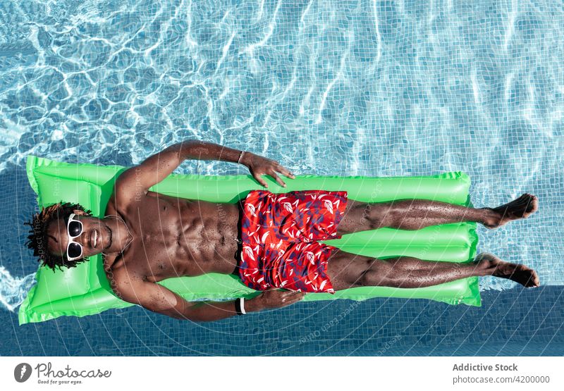 Schwarzer Mann entspannt sich auf aufblasbarer Matratze im Pool Schlafmatratze sich[Akk] entspannen sorgenfrei Sommer Urlaub genießen Lächeln männlich ethnisch