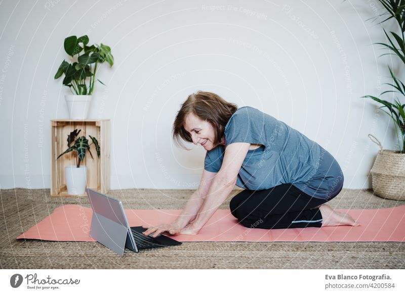 Nahaufnahme von reifen kaukasischen Senior Frau übt Yoga-Pose zu Hause. mit Laptop für Online-Klasse mit Lehrer. Gesunde und Technologie Lebensstil Seniorin