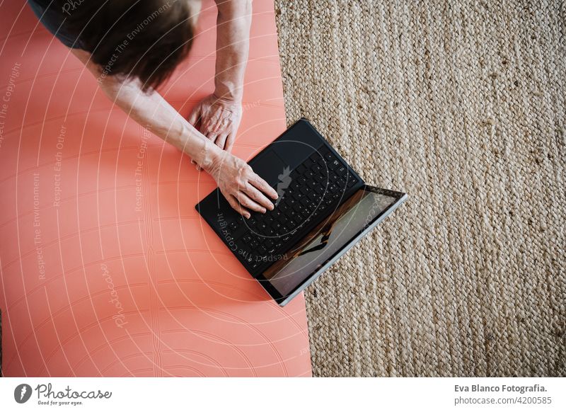 Nahaufnahme von reifen kaukasischen Senior Frau übt Yoga-Pose zu Hause. mit Laptop für Online-Klasse mit Lehrer. Gesunde und Technologie Lebensstil Seniorin