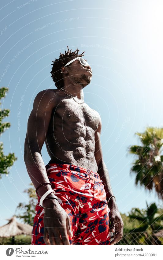 Muskulöser schwarzer Mann mit Sonnenbrille nach dem Training im Freibad Schwimmer ohne Hemd muskulös Athlet Beckenrand selbstbewusst Wellness Sportler