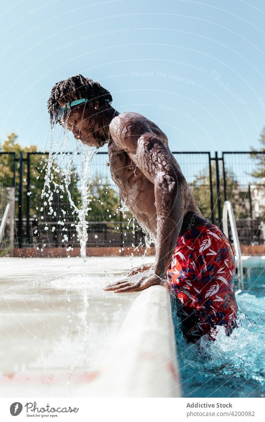 Schwarzer Mann spritzt Wasser im Pool platschen Beckenrand fettarm auftauchen nass Sommer Urlaub männlich ethnisch schwarz Afroamerikaner schwimmen Aktivität