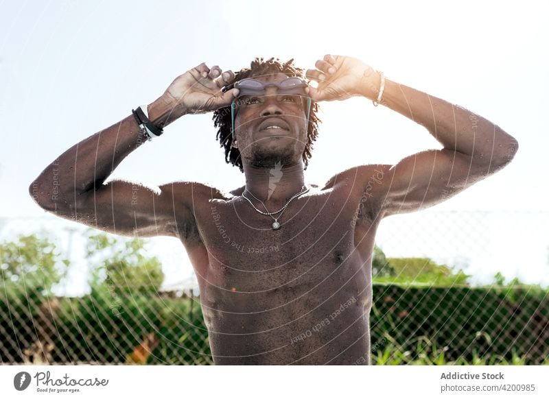 Muskulöser schwarzer Mann, der seine Schwimmbrille nach dem Training im Freibad einstellt Schwimmer ohne Hemd muskulös Athlet Beckenrand ausrichten Schutzbrille
