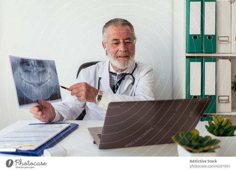 Zahnarzt zeigt auf Röntgenbild während Videogespräch auf Laptop Kieferorthopäde Video-Chat online Gesundheitswesen Beratung mündlich Mann benutzend Apparatur