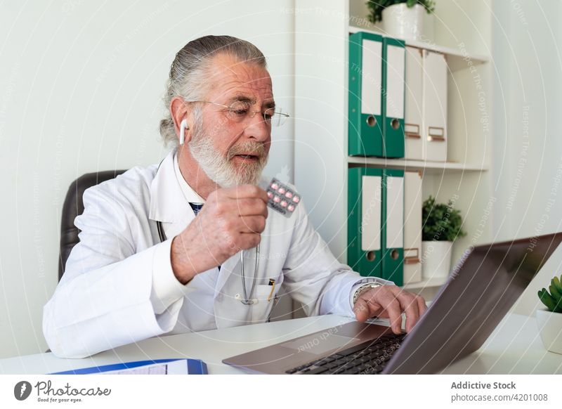 Arzt mit Tabletten während eines Videogesprächs am Laptop in der Klinik Videoanruf Medikament sprechen Beratung Entfernung Mann Apparatur Blister Rudel Pharma