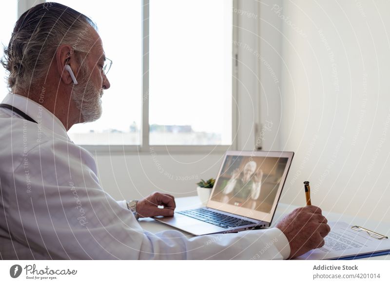 Arzt im Gespräch mit dem Patienten per Videochat auf dem Laptop geduldig Videoanruf abgelegen Beratung online Bildschirm Mann benutzend Apparatur Ohrstöpsel