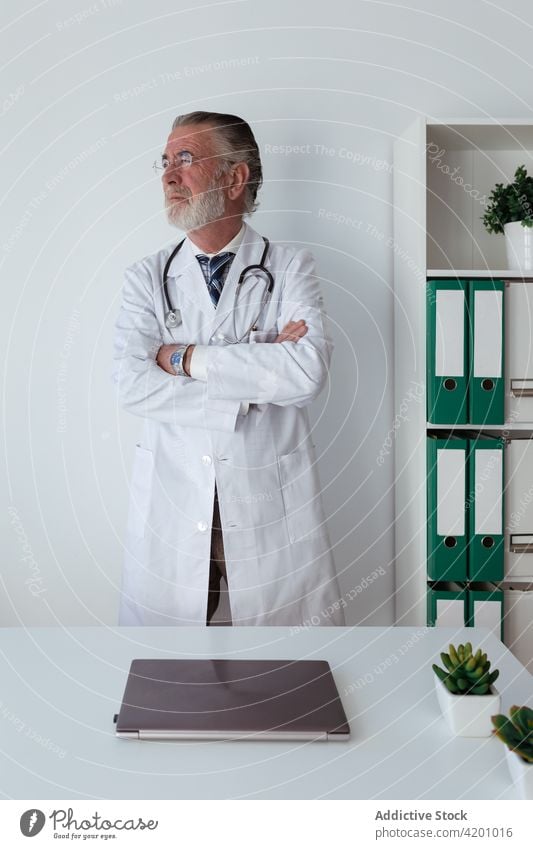 Älterer Arzt mit verschränkten Armen im Krankenhaus arzt die Arme verschränkt selbstsicher professionell Spezialist Uniform Stethoskop Mann Klinik Porträt Robe