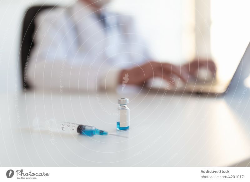 Ein Arzt tippt auf einem Laptop in der Nähe von Impfstoff und Spritze Tippen wissenschaftlich Biologie Tisch Klinik benutzend Apparatur Gerät klein Flasche