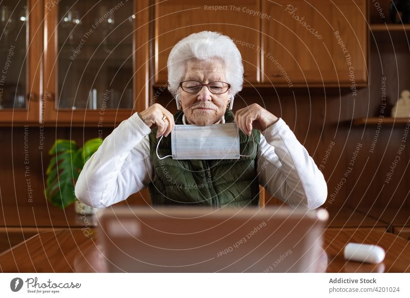 Ältere Frau zeigt während eines Videogesprächs eine sterile Maske auf ihren Laptop Mundschutz Videoanruf Gesundheitswesen Beratung online behüten benutzend