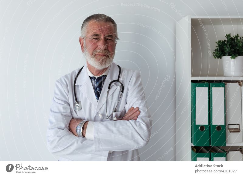Älterer Arzt mit verschränkten Armen im Krankenhaus arzt die Arme verschränkt selbstsicher professionell Spezialist Uniform Stethoskop Mann Klinik Porträt Robe