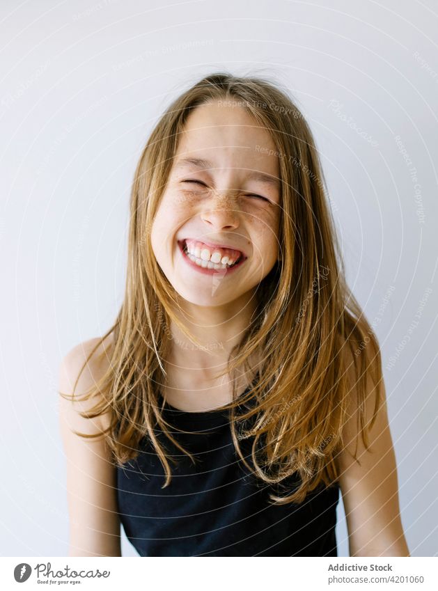 Glückliches Mädchen mit langen Haaren und Sommersprossen vor weißem Hintergrund Kind Lachen heiter aufgeregt Porträt Spaß Freude Humor positiv
