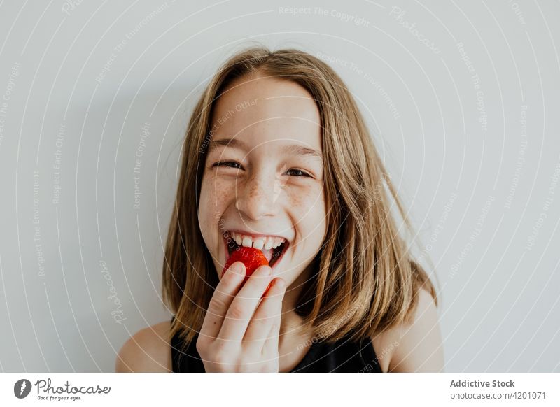 Aufgeregtes Mädchen isst Erdbeere und lächelt essen Erdbeeren Lächeln lecker Freude genießen Frucht Beeren Porträt heiter Biss Optimist Lebensmittel froh süß