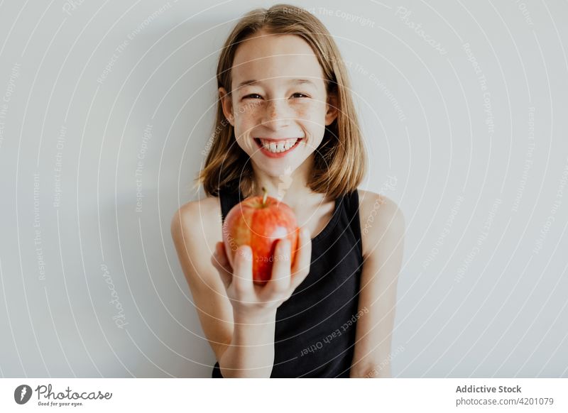 Entzücktes Kind beißt Apfel gegen weiße Wand Mädchen Biss heiter Lächeln essen frisch Frucht Vitamin genießen Porträt Mahlzeit Freude Glück reif lässig Top