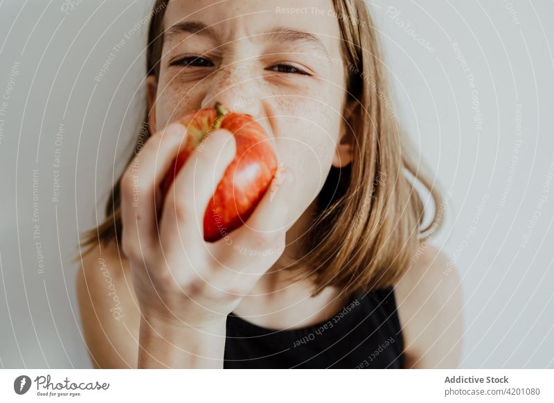 Entzücktes Kind beißt Apfel gegen weiße Wand Mädchen Biss essen frisch Frucht Vitamin genießen Porträt Mahlzeit Freude reif lässig Top Menschliches Gesicht