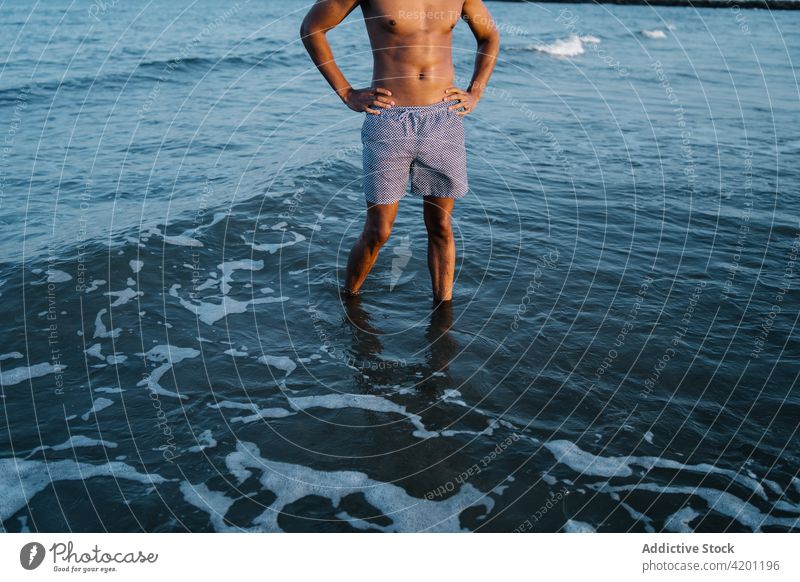 Anonymer schwarzer Tourist im Meer während einer Sommerreise Urlaub Hand auf der Taille nackter Torso reisen Natur Himmel Mann Afroamerikaner schaumig wellig