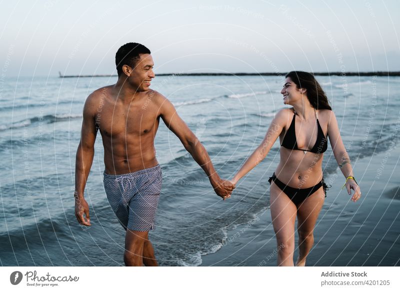 Schönes vielfältiges Paar, das sich beim Spazierengehen am Strand an den Händen hält Händchenhalten Partnerschaft Liebe romantisch Tourismus Urlaub MEER