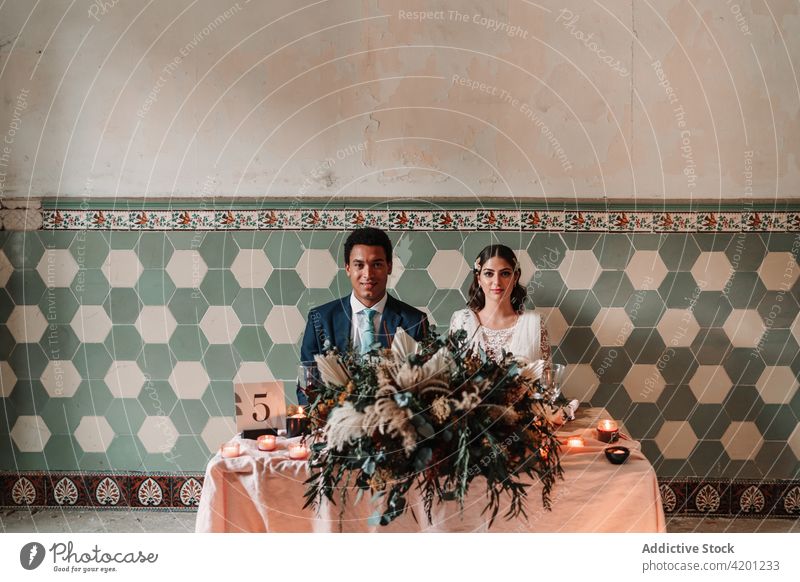 Multiethnisches frisch vermähltes Paar am Tisch mit Dekoration am Hochzeitstag Jungvermählter Heirat Dekoration & Verzierung Partnerschaft festlich feiern