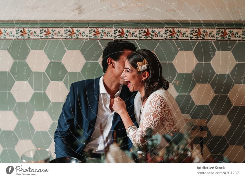 Nicht erkennbarer schwarzer Bräutigam flüstert in das Ohr der lächelnden Braut in einem Haus striegeln hauchen Hochzeit Liebe altehrwürdig Partnerschaft feiern