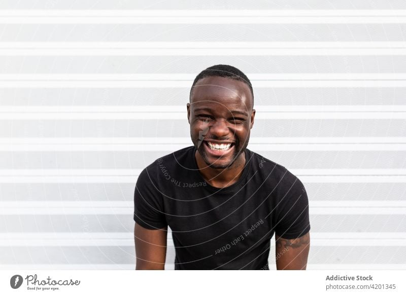 Fröhliches schwarzes Männchen in der Nähe der gestreiften Wand stehend Mann heiter herzlich Freundschaft Glück Porträt Streifen Inhalt froh männlich Lächeln
