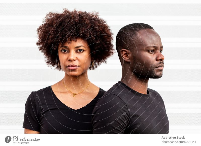 Seriöses schwarzes Paar in der Nähe der gestreiften Wand bei Tag ernst herzlich Partnerschaft lässig Stil wehmütig Afro-Look Porträt Streifen Ornament Frisur