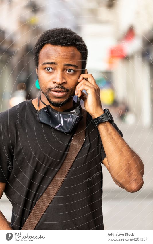 Lächelnder schwarzer Mann, der auf einer Straße in der Stadt mit seinem Smartphone spricht sprechen freundlich maskulin Gespräch Porträt benutzend Apparatur