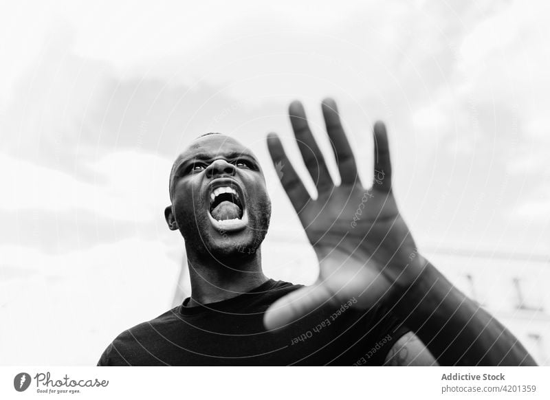 Aggressiver schwarzer Demonstrant schreit auf einer Straße in der Stadt Protestierender Schrei stoppen angriffslustig wütend BLM auflehnen Mann Porträt