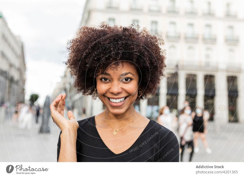 Lächelnde schwarze Frau auf städtischem Bürgersteig bei Tag heiter offen freundlich charmant Afro-Look Frisur Straße Großstadt Porträt Afroamerikaner urban