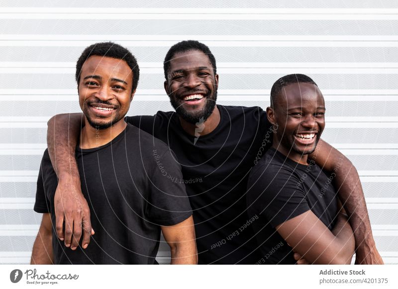Fröhliche schwarze männliche Freunde umarmen sich in der Nähe der gestreiften Wand bester Freund Umarmen heiter herzlich Freundschaft Glück BLM Bewegung Männer