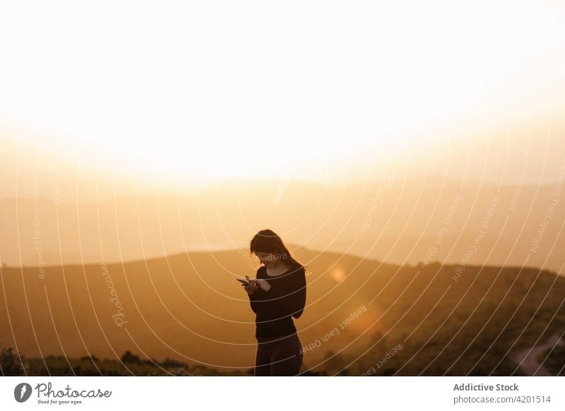 Zufriedene Frau mit Smartphone in den Bergen bei Sonnenuntergang Berge u. Gebirge Browsen Freiheit genießen Hochland Hügel heiter Internet online Gerät Telefon