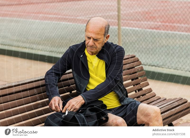 Älterer Mann bereitet sich auf Tennistraining vor Sportler Tasche offen Gericht vorbereiten Bank Training sitzen männlich Senior gealtert älter Sportbekleidung