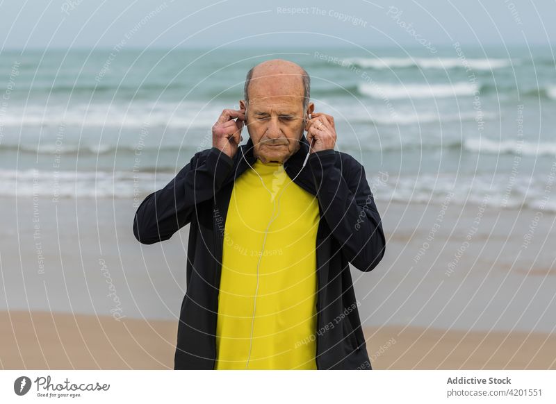 Seniorensportler, der sich am Meer Kopfhörer aufsetzt Sportler angezogen Training Fitness Strand MEER zuhören Musik männlich Athlet gealtert älter Lifestyle