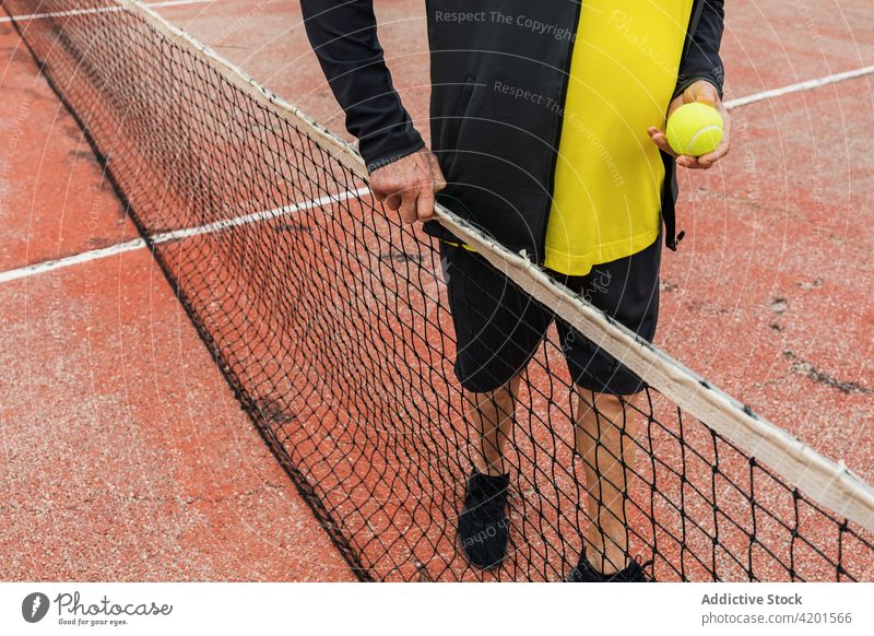Crop Senior Tennisspieler in der Nähe des Netzes Sportler Gericht Ball Training Aktivität Spiel Streichholz männlich älter gealtert schäbig verwittert Athlet