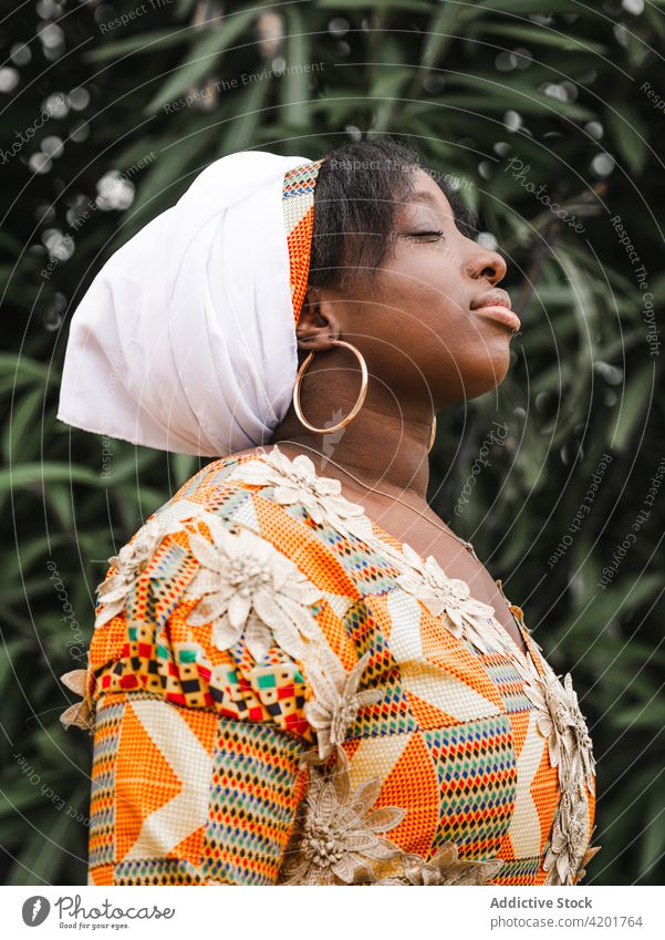 Verträumte schwarze Frau in traditionellem Outfit im Garten Augen geschlossen verträumt atmen Stil charmant Windstille Porträt Profil feminin elegant Ornament