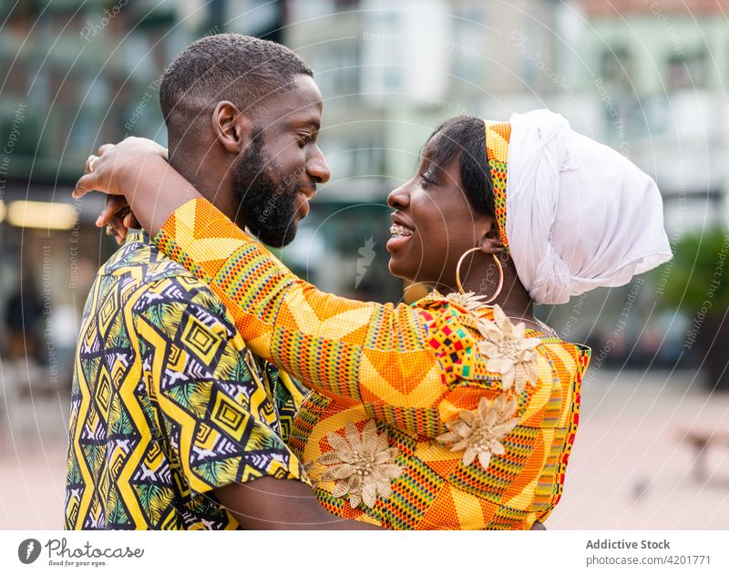 Glückliches ethnisches Paar, das sich auf einer Straße in der Stadt umarmt Umarmen reden Partnerschaft Liebe Romantik Seelenverwandter Ornament Straßenbelag