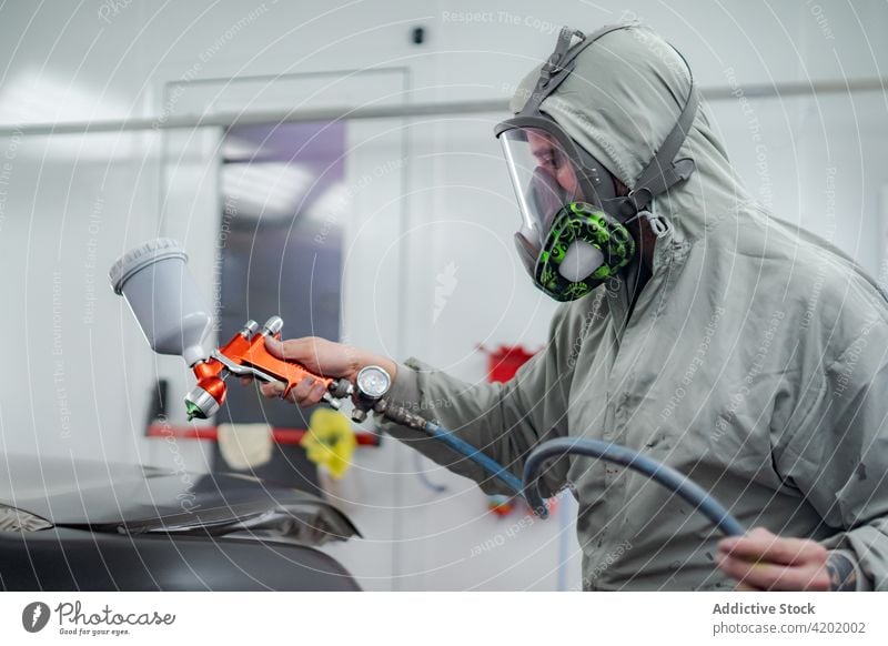 Mann in Arbeitskleidung lackiert Auto in Werkstatt Farbe Pistole PKW Aerosol Spray Atemschutzgerät behüten Arbeiter Automobil männlich Mundschutz Meister Anzug