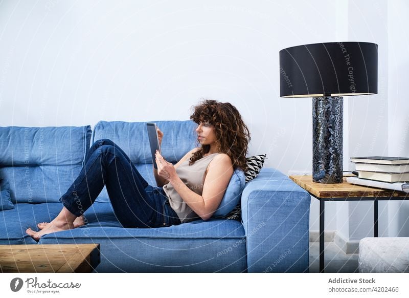 Junge Frau benutzt ein Tablet, während sie sich auf der Couch ausruht Lügen Browsen Sofa Tablette Raum benutzend Liege Surfen Internet sich[Akk] entspannen
