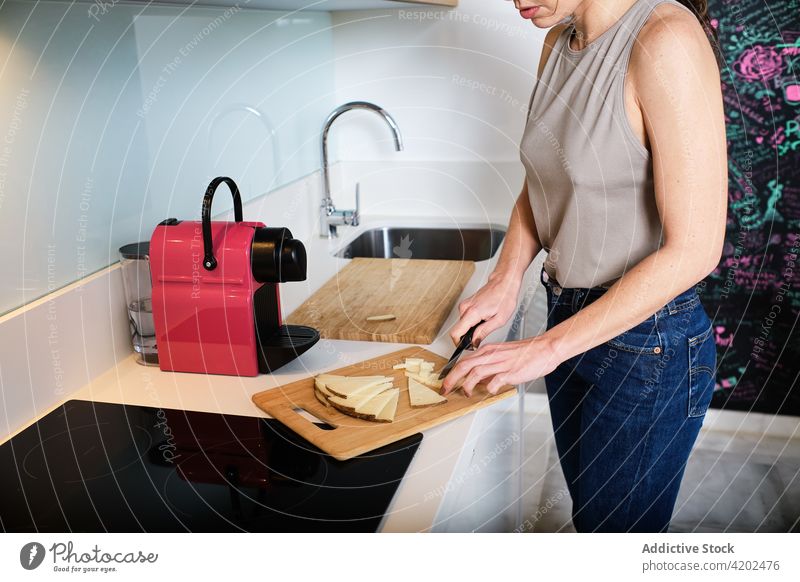 Anonyme Frau schneidet Käse in der Küche geschnitten Abfertigungsschalter Koch Schneidebrett Kabinett Wasserhahn Kreide Wand heimwärts vorbereiten modern