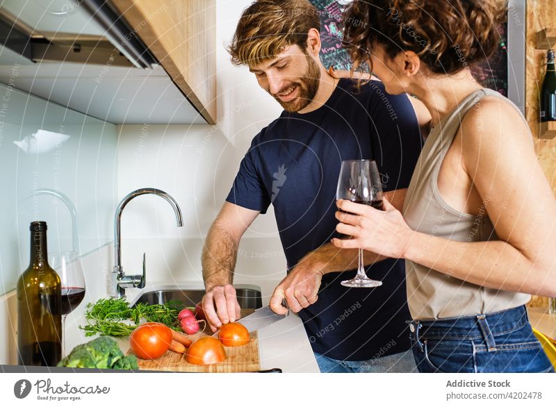 Ehepaar in der Küche mit Weinglas beim Schneiden von Gemüse Paar Koch Tomate geschnitten trinken Freund Abfertigungsschalter Lifestyle jung Kabinett heimwärts