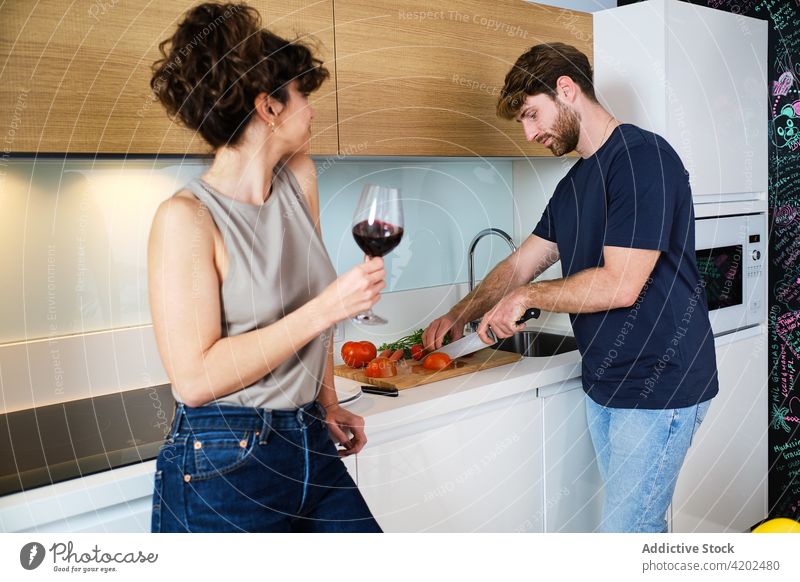 Ehepaar in der Küche mit Weinglas beim Schneiden von Gemüse Paar Koch Tomate geschnitten trinken Freund Abfertigungsschalter Lifestyle jung Kabinett heimwärts