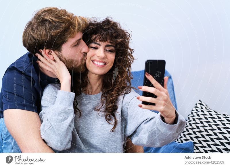 Glückliches Paar macht Selfie mit Smartphone Zusammensein Kuss heiter Lächeln Liebe Selbstportrait Mobile Telefon lässig benutzend Moment Umarmung Umarmen