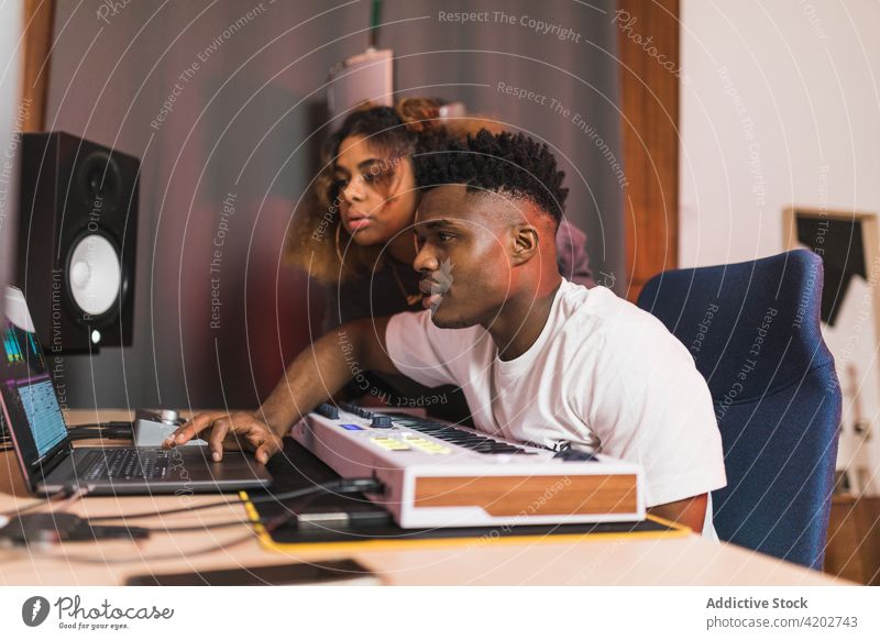Schwarze Freunde teilen sich einen Laptop mit einem Aufnahmeprogramm auf dem Bildschirm Software achtsam Produzent Musik Atelier benutzend Apparatur Gerät