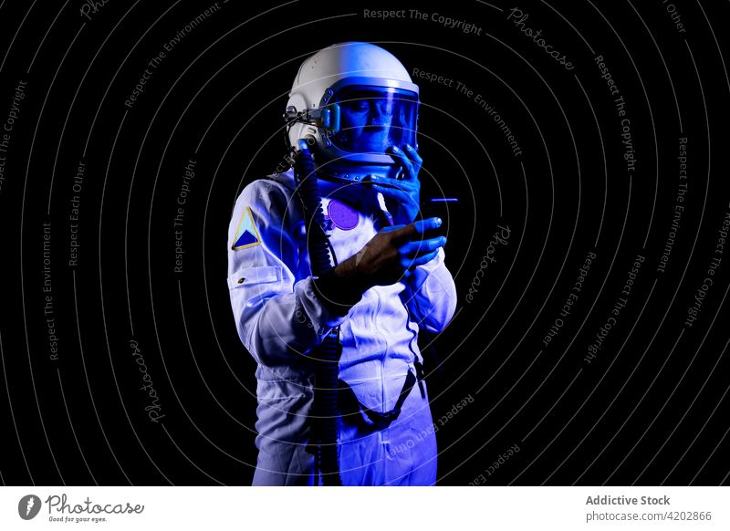 Astronaut im Raumanzug mit Smartphone auf schwarzem Hintergrund Mann benutzend Browsen Panzerung Astronomie Apparatur professionell ernst Kosmonaut schützend